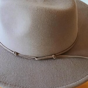 May include: A light brown fedora-style hat with a wide brim and a matching band around the crown. The hat has a soft, felt-like texture and a classic, timeless design. The hat is suitable for various occasions.