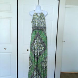 May include: A floor-length sleeveless maxi dress featuring a green, white, and black paisley pattern. The garment has a high halter neckline, a defined waistband with a geometric border, and a flowing skirt with a repeating diamond-shaped motif.
