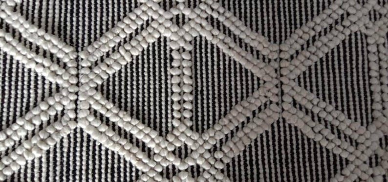May include: A black and white textured rug with a diamond pattern. The rug is made of woven fabric with raised white circles.Chunky weave wool rug, natural wool rug, mix weave wool rug, boho home decor rug, indoor rug,