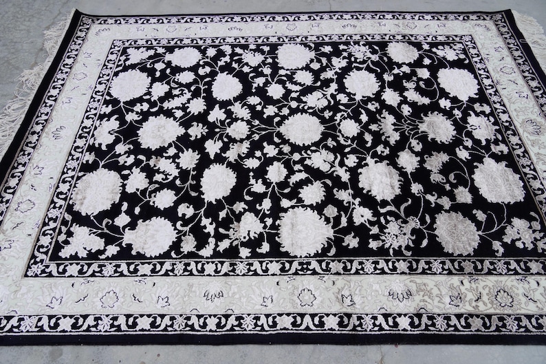 A 5.5x7.9 ft hand-knotted rug featuring a large, ornate ivory and blue central medallion on a deep navy blue field. The field is filled with intricate scrolling vines and small floral motifs. A wide, multi-layered border in ivory and light blue frames the rug. The rug is made of wool with silk highlights that give it a subtle sheen, finished with a short white fringe at the top and bottom.