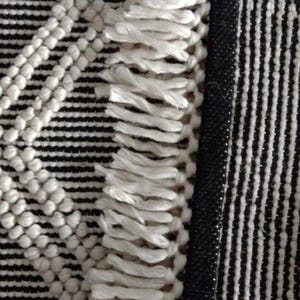 May include: A black and white woven rug with a fringe border. The rug has a geometric pattern with white circles and a diamond shape in the center.Chunky weave wool rug, natural wool rug, mix weave wool rug, boho home decor rug, indoor rug,