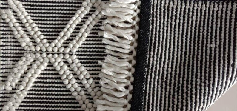 May include: A black and white woven rug with a fringe border. The rug has a geometric pattern with white circles and a diamond shape in the center.Chunky weave wool rug, natural wool rug, mix weave wool rug, boho home decor rug, indoor rug,