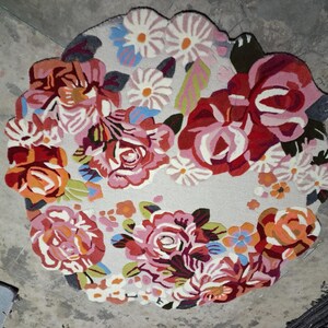 Round hand-tufted wool rug with a vibrant floral pattern in pink, red, orange, and white on a pale background; textured modern living room rug.
