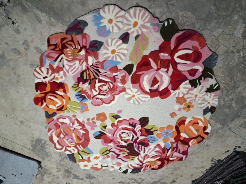 Round hand-tufted wool rug with a vibrant floral pattern in pink, red, orange, and white on a pale background; textured modern living room rug.