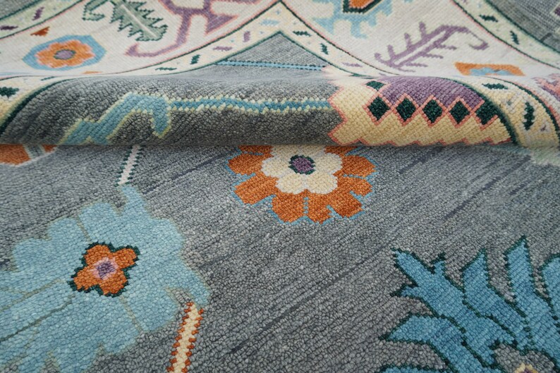 Hand-knotted wool rug in floral Turkish Oushak style, 8x10; blue-gray field with teal, rust, and peach blossoms.