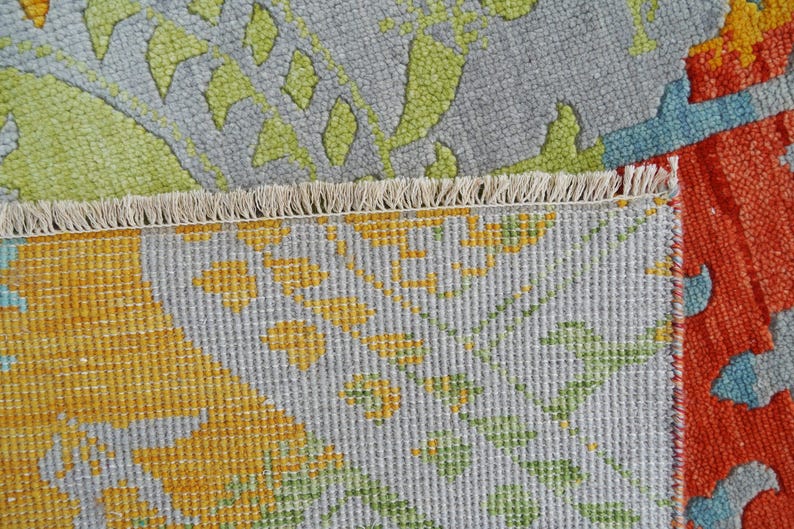 Hand-knotted wool Oushak rug in paisley pattern; rolled samples in teal, blue, orange for a textured floor decor rug.