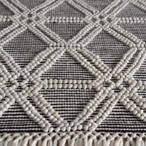 May include: A white and black geometric rug with a diamond pattern. The rug has a fringe border and is made of a textured material.Chunky weave wool rug, natural wool rug, mix weave wool rug, boho home decor rug, indoor rug,