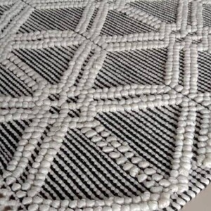 May include: A black and white woven rug with a geometric pattern and fringe edges. The rug has a textured, raised surface.Chunky weave wool rug, natural wool rug, mix weave wool rug, boho home decor rug, indoor rug,