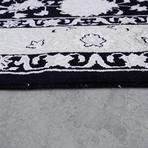 A 5.5x7.9 ft hand-knotted rug featuring a large, ornate ivory and blue central medallion on a deep navy blue field. The field is filled with intricate scrolling vines and small floral motifs. A wide, multi-layered border in ivory and light blue frames the rug. The rug is made of wool with silk highlights that give it a subtle sheen, finished with a short white fringe at the top and bottom.