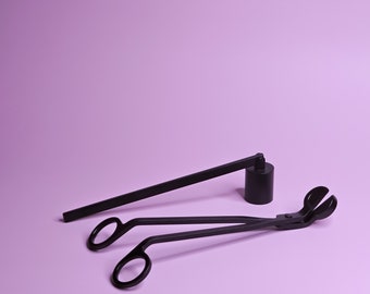 Könnte beinhalten: Schwarzes Kerzenzubehör-Set auf lila Hintergrund. Das Set beinhaltet einen Docht-Dipper, einen Docht-Trimmer und einen Kerzenlöscher. Die Werkzeuge sind aus Metall gefertigt und haben ein mattes Finish. Artikel zur Kerzenpflege.