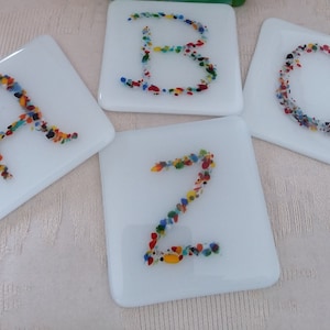 May include: Four white square coasters with the letters A, B, C, and Z spelled out in colorful mosaic-like designs.
