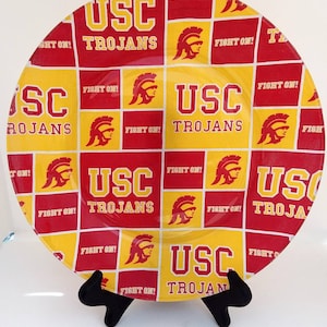 May include: A round glass plate with a red and yellow checkered pattern. The plate features the USC Trojans logo, including the words "USC Trojans" and "Fight On!" repeated throughout the design.