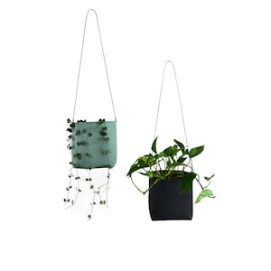 May include: Two hanging plant pots, one green and one black, with plants growing out of them. The pots are made of fabric and have a simple design.