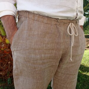 Puede incluir: Pantalones de lino color beige con cintura con cord&oacute;n. Los pantalones tienen un corte holgado y bolsillos. El modelo lleva una camisa de lino blanca. Los pantalones est&aacute;n hechos de una tela texturizada.