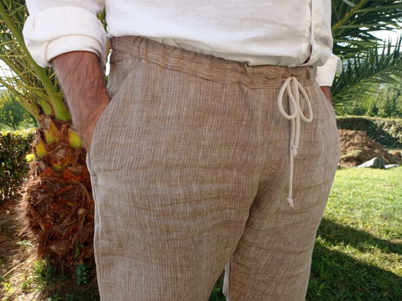 Puede incluir: Pantalones de lino color beige con cintura con cord&oacute;n. Los pantalones tienen un corte holgado y bolsillos. El modelo lleva una camisa de lino blanca. Los pantalones est&aacute;n hechos de una tela texturizada.