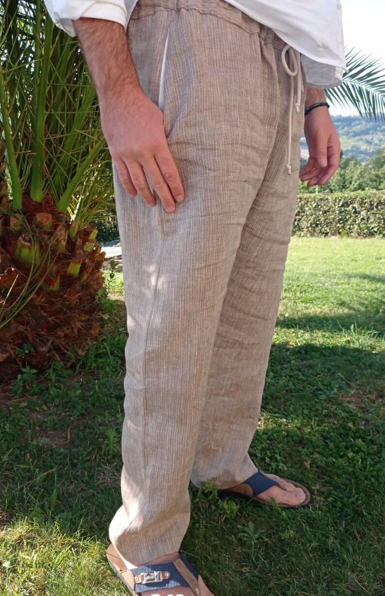 Puede incluir: Pantalones de lino color beige con cintura con cord&oacute;n y bolsillos laterales. Los pantalones son de color neutro y parecen ligeros. La persona lleva sandalias. Adecuados para uso casual.