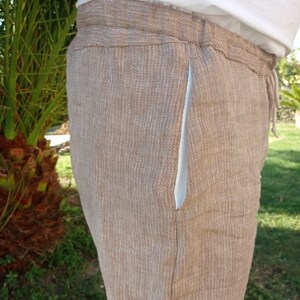Puede incluir: Pantalones de lino color beige con cintura con cord&oacute;n y forro de bolsillo azul claro. Los pantalones est&aacute;n hechos de una tela texturizada y parecen ligeros. Los pantalones son parte de una colecci&oacute;n de ropa casual.