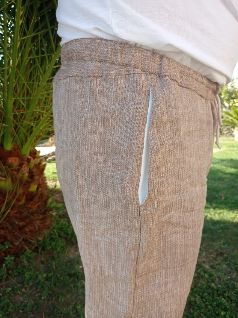 Puede incluir: Pantalones de lino color beige con cintura con cord&oacute;n y forro de bolsillo azul claro. Los pantalones est&aacute;n hechos de una tela texturizada y parecen ligeros. Los pantalones son parte de una colecci&oacute;n de ropa casual.