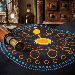 以下が含まれることがあります： 黒い布地に、カラフルな円形の刺繍が施されています。デザインは、青、オレンジ、赤の色合いの同心円になっています。