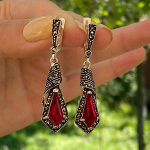 May include: A pair of silver dangle earrings with red gemstone accents and marcasite detailing.