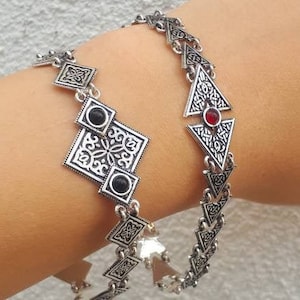 May include: Two silver bracelets with intricate geometric designs. One bracelet features a black stone and the other features a red stone.