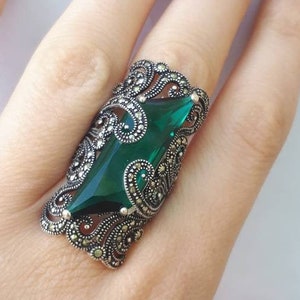 May include: A silver ring with a large, emerald green gemstone set in a filigree design.