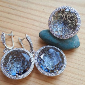 May include: A set of silver earrings and a ring with blue crystal stones surrounded by a silver halo of smaller stones.