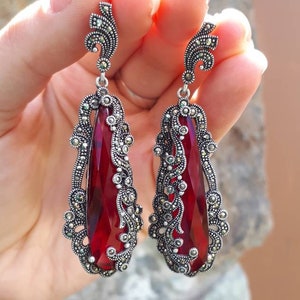 Puede incluir: Un par de pendientes de plata con piedras rojas en forma de lágrima y diseños filigranados intrincados.