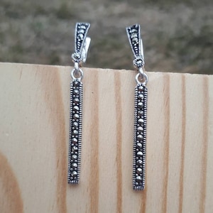 May include: A pair of silver dangle earrings with a long, thin bar design. The bar is adorned with small, round, black marcasite stones.