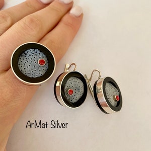 Op de afbeelding: Een set zilveren oorbellen en een ring met zwarte en witte gepatroneerde cirkels en een rode stip in het midden. De sieraden zijn gemarkeerd met "ArMat Silver".