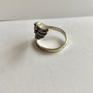 May include: Silver ring with a detailed wing design. The ring is open on one side and has a textured band.