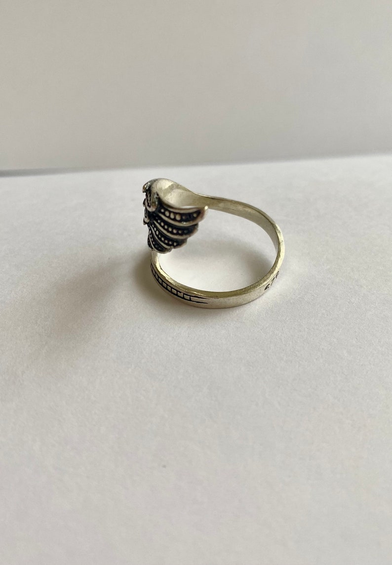 May include: Silver ring with a detailed wing design. The ring is open on one side and has a textured band.