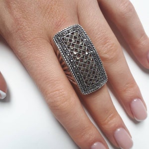 Könnte beinhalten: Ein silberner Ring mit einem rechteckigen Design, das ein geometrisches Muster aus schwarzen Markasit-Steinen aufweist.