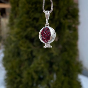 May include: A silver necklace with a pomegranate pendant. The pendant is filled with red gemstones.