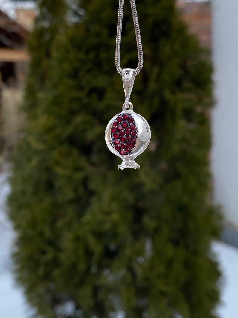May include: A silver necklace with a pomegranate pendant. The pendant is filled with red gemstones.