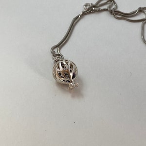 May include: A silver chain necklace with a silver pendant shaped like a pomegranate. The pendant is openwork and has a delicate design.