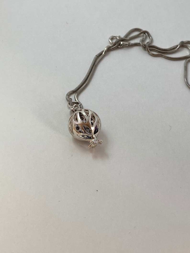 May include: A silver chain necklace with a silver pendant shaped like a pomegranate. The pendant is openwork and has a delicate design.