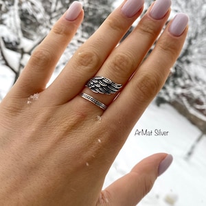 May include: A silver ring with an angel wing design. The ring is on a finger with a plain silver band underneath. The text "ArMat Silver" is visible in the lower right corner of the image.
