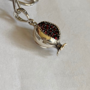 May include: A silver necklace with a pomegranate pendant. The pendant is decorated with red gemstones.