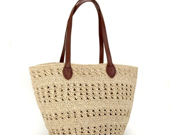 May include: A beige crocheted tote bag with brown leather handles. The bag has a wide, open top and a rounded bottom.