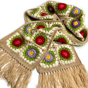 May include: A crocheted scarf with a fringe, featuring a pattern of colorful flowers in shades of red, green, yellow, purple, and white.