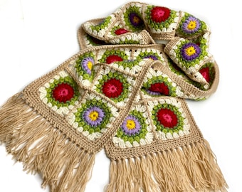 May include: A crocheted scarf with a fringe, featuring a pattern of colorful flowers in shades of red, green, yellow, purple, and white.