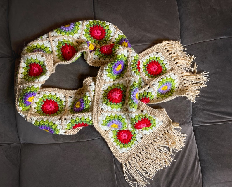 May include: A crocheted scarf with a fringe, featuring a floral pattern in shades of red, green, white, and purple.