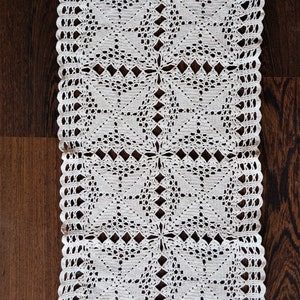 May include: White crocheted doily with a delicate pattern of squares and diamonds. The doily is made of cotton thread and has a scalloped edge.