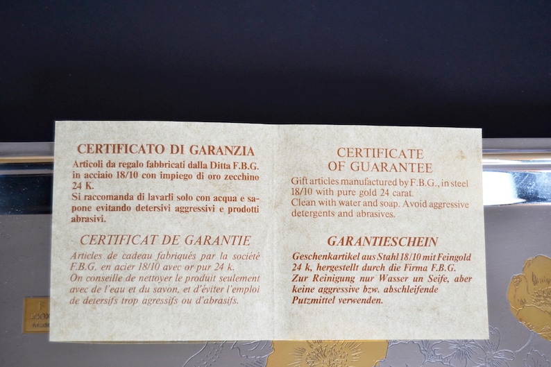 May include: A warranty certificate for gift articles made of steel with 24 karat gold. The certificate is printed in Italian, French, English, and German. It recommends cleaning with water and soap and avoiding aggressive detergents and abrasives.