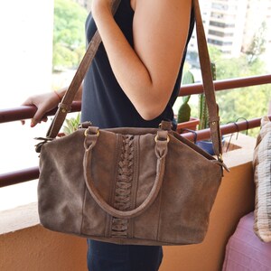 Pode incluir: Uma bolsa de mão de camurça marrom com um detalhe trançado e uma alça longa. A bolsa tem uma alça superior e um fecho de correr.