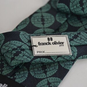 May include: A dark blue and green patterned silk tie with a white tag that reads "franck olivier paris" and "PRIX___".