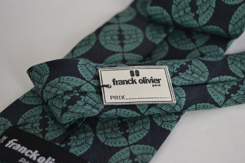 May include: A dark blue and green patterned silk tie with a white tag that reads "franck olivier paris" and "PRIX___".
