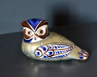 May include: A ceramic owl figurine with blue, brown, and white painted details. The owl is sitting on a silver surface.