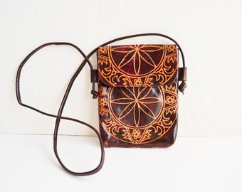 May include: A brown leather crossbody bag with a floral design. The bag has a flap closure and a long strap.